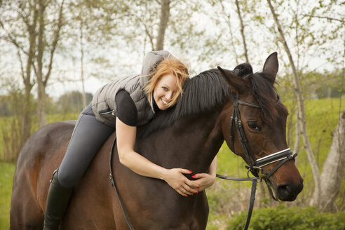 Lächelnde junge Frau auf einem Pferd - FCF01196