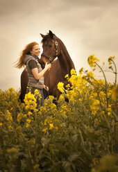 Porträt einer glücklichen jungen Frau mit ihrem Pferd in einem Rapsfeld - FCF01198