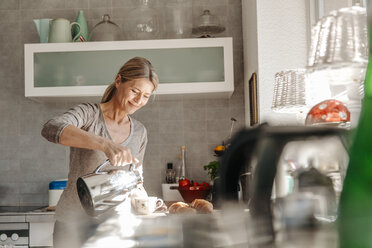 Frau zu Hause in der Küche gießt Kaffee in eine Tasse - JOSF00769