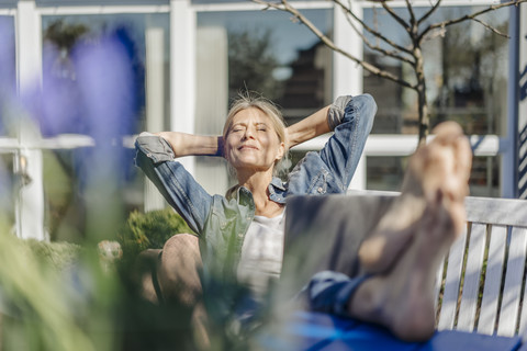 Lächelnde Frau mit Laptop entspannt sich auf einer Gartenbank, lizenzfreies Stockfoto