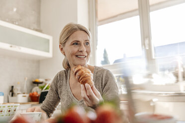 Frau isst zu Hause ein Croissant - JOSF00783