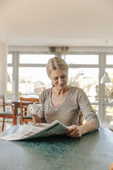 Frau zu Hause am Tisch sitzend mit einer Tasse Kaffee und einer Zeitung - JOSF00795