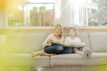 Mature woman and girl at home looking at photo album on couch - JOSF00796