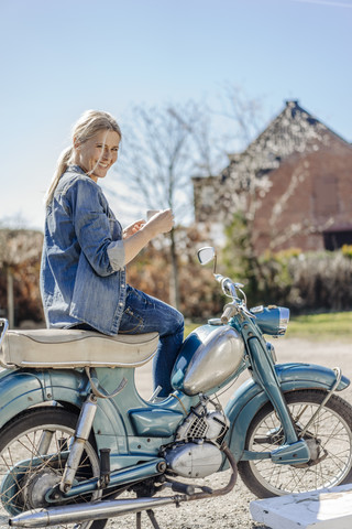 Lächelnde Frau auf altem Motorrad bei einer Kaffeepause, lizenzfreies Stockfoto