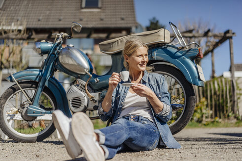 Lächelnde Frau sitzt auf einem alten Motorrad und macht eine Kaffeepause - JOSF00814