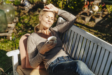 Frau mit Tasse Kaffee entspannt auf Gartenbank - JOSF00817
