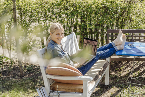 Lächelnde Frau mit Laptop auf einer Gartenbank - JOSF00818