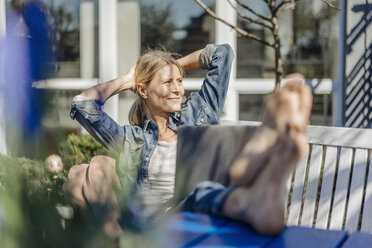 Lächelnde Frau mit Laptop entspannt sich auf einer Gartenbank - JOSF00819