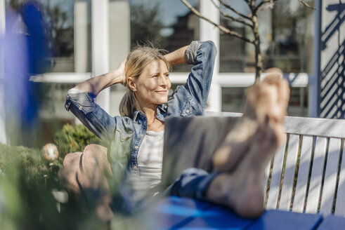 Lächelnde Frau mit Laptop entspannt sich auf einer Gartenbank - JOSF00819