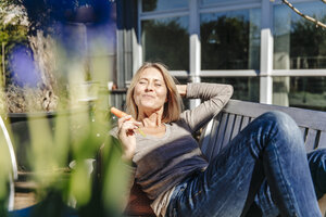 Woman relaxing on garden bench eating a carrot - JOSF00820