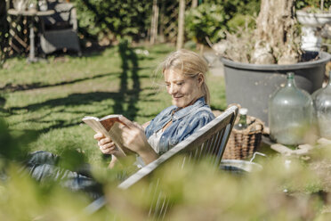 Lächelnde Frau, die auf einer Gartenbank ein Buch liest - JOSF00823