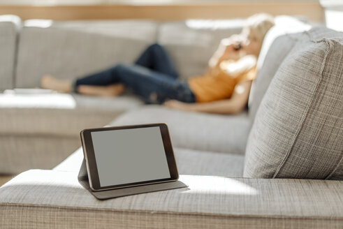 Tablet auf Couch mit entspannter Frau im Hintergrund - JOSF00825