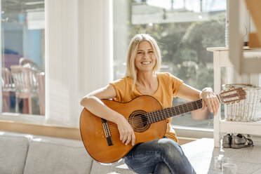 Lächelnde Frau zu Hause mit Gitarre - JOSF00830
