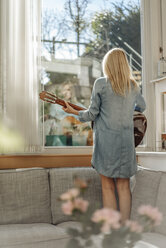 Woman at home standing on couch looking out of window - JOSF00838
