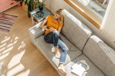 Frau zu Hause auf der Couch mit Mobiltelefon - JOSF00849