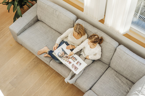 Reife Frau und Mädchen zu Hause mit Blick auf Fotoalbum auf Couch, lizenzfreies Stockfoto