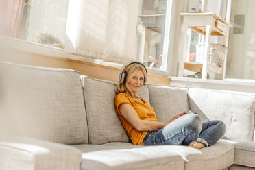 Woman at home sitting on couch wearing headphones - JOSF00870