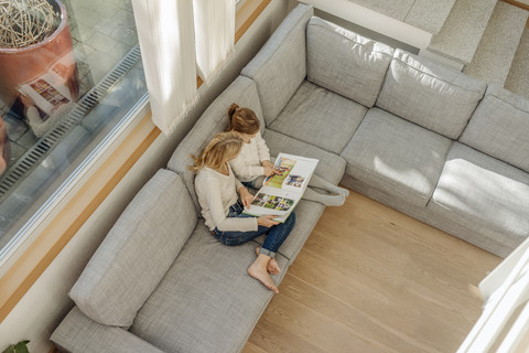 Reife Frau und Mädchen zu Hause mit Blick auf Fotoalbum auf Couch, lizenzfreies Stockfoto