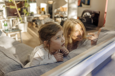 Mature woman and girl at home on couch looking out of window stock photo