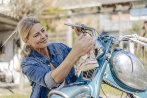 Lächelnde Frau beim Reinigen eines alten Motorrads - JOSF00904