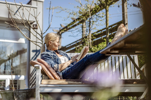 Smiling woman reading book on garden bench stock photo