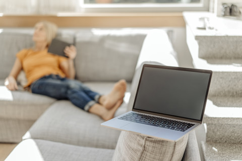 Laptop auf Couch mit Frau im Hintergrund, lizenzfreies Stockfoto