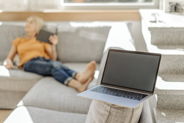 Laptop auf Couch mit Frau im Hintergrund - JOSF00916