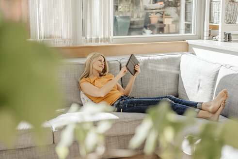Frau zu Hause auf der Couch mit einer Tasse Kaffee und einem Tablet - JOSF00917