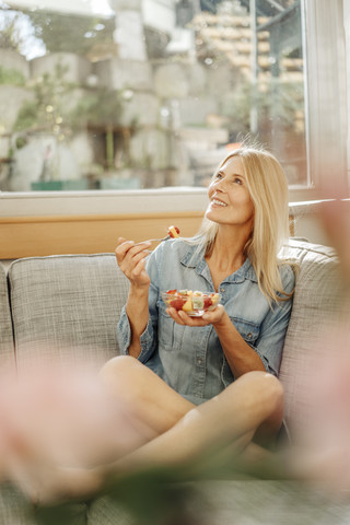 Woman at home sitting on couch eating fruit salad stock photo