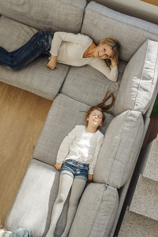 Happy mature woman and girl at home lying on couch stock photo