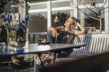 Woman wearing headphones relaxing on garden bench - JOSF00951