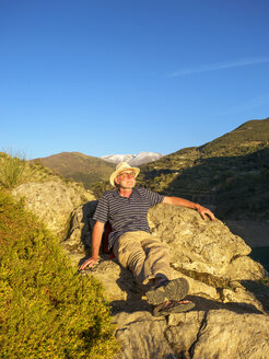 Spain, Gueejar Sierra, senior man sitting on rocks enjoying evening sunlight - LAF01842