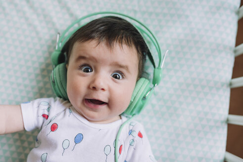 Porträt eines kleinen Mädchens mit Kopfhörern, das in einem Kinderbett liegt - GEMF01609