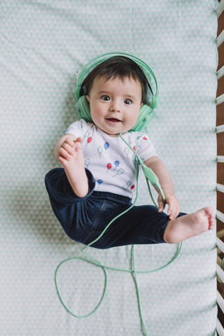 Porträt eines kleinen Mädchens, das in einem Kinderbett liegt und mit Kopfhörern Musik hört, lizenzfreies Stockfoto