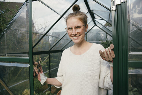 Portrait of smiling young woman standing in the door of her greenhouse - MFF03486