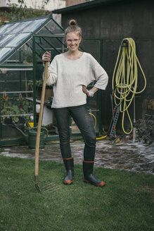 Porträt einer lächelnden jungen Frau, die mit einer Harke im Garten steht - MFF03492