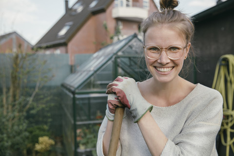 Porträt einer lächelnden jungen Frau mit Harke im Garten, lizenzfreies Stockfoto