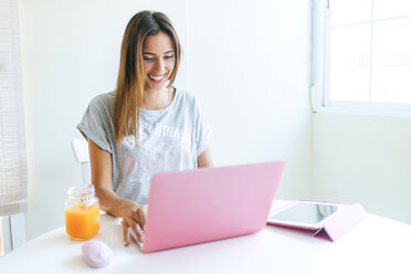 Lächelnde junge Frau bei der Arbeit mit Laptop und Tablet zu Hause - KIJF01468