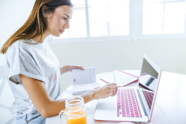 Junge Frau arbeitet zu Hause mit Laptop und Tablet - KIJF01474