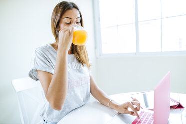 Junge Frau trinkt Orangensaft und benutzt einen Laptop - KIJF01475