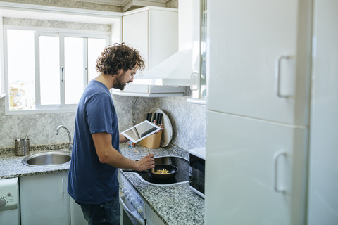 Man cooking in kitchen while looking at tablet stock photo