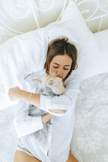 Woman lying on bed with hugging and kissing her Yorkshire Terrier, top view - KIJF01492