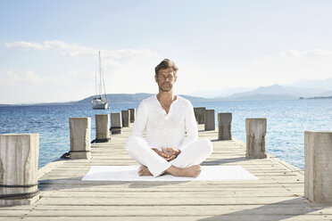 Mature man doing yoga exercise on jetty - PDF01231