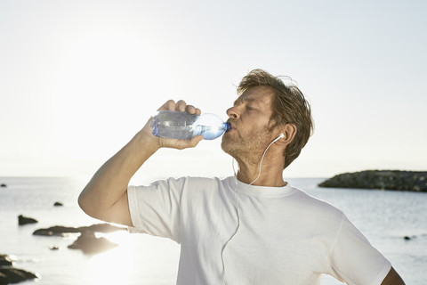 Älterer Mann trinkt Wasser nach dem Joggen am Strand, lizenzfreies Stockfoto