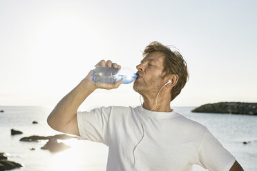 Älterer Mann trinkt Wasser nach dem Joggen am Strand - PDF01248