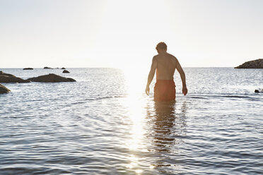 Rückenansicht eines im Meer stehenden Mannes bei Sonnenuntergang - PDF01251