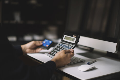 Man using calculator and credit card at desk, partial view - JPF00196