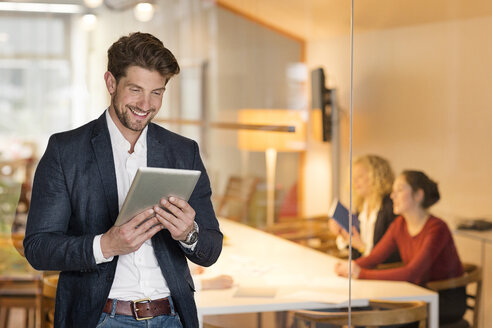 Junger Geschäftsmann im Büro, der ein digitales Tablet benutzt, mit Kollegen im Hintergrund - PESF00565