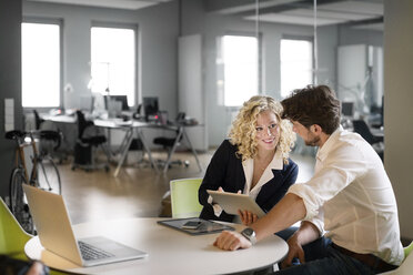 Businessman and woman discussing project in office, using digital tablet - PESF00575