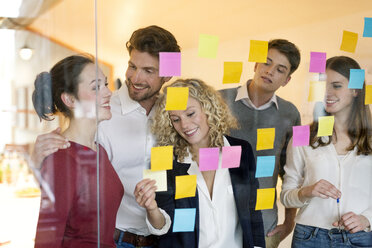 Business people discussing in front of glass screen with sticky notes - PESF00576